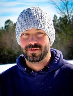 a man with a beard wearing a knitted hat and blue jacket in the snow