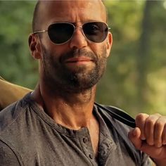 a bald man wearing sunglasses holding a knife in his right hand and looking at the camera