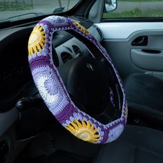 the steering wheel cover is crocheted with sunflowers in purple and yellow