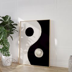 a black and white painting sitting on top of a wooden floor next to a potted plant