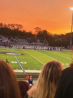 the sun sets over a football field as people watch from the bleachers at sunset