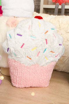 a white cupcake pillow sitting on top of a wooden floor next to a stuffed animal