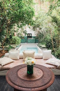 a patio with couches, pillows and a table in front of a swimming pool