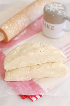 a piece of bread sitting on top of a table next to a mug and rolling pin