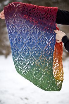 a woman holding up a multicolored shawl in the snow with her hands