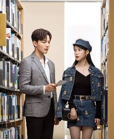 a man and woman standing next to each other in front of a book shelf filled with books