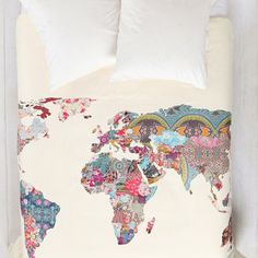 an image of a bed with white sheets and colorful world map on the coverlet