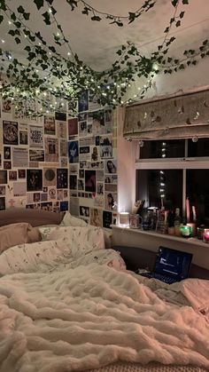 an unmade bed with lots of pictures on the wall and lights hanging from the ceiling