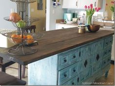 a kitchen island made out of an old dresser with fruit bowls on it and flowers in the vases