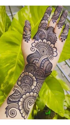 a hand with henna tattoos on it and some plants in the backgroud