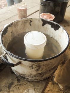 a bucket filled with water sitting on top of a wooden table next to other pots