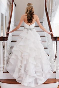 a woman in a white wedding dress standing on stairs with her hands on the railing