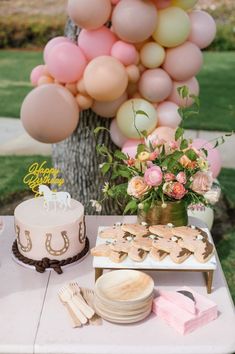 a table topped with a cake next to a tree filled with pink and white balloons