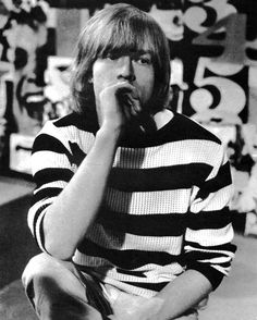 a man sitting on the floor eating something with his hand in his mouth and wearing a striped shirt