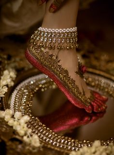 a woman's feet in gold and red shoes with jewels on the bottom, surrounded by flowers