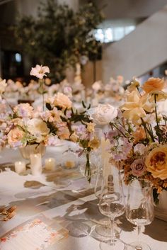 an arrangement of flowers in vases on a long table with candles and napkins