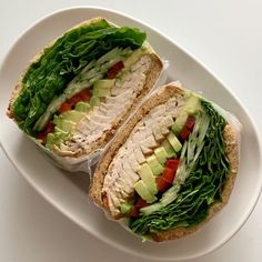 two sandwiches with lettuce, tomato and avocado on a white plate