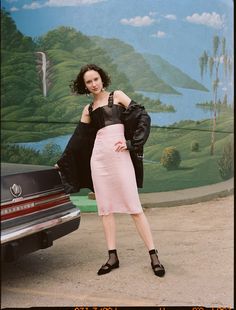 a woman standing next to a parked car in front of a wall with a painting on it