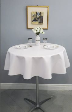 a white table with two glasses and flowers on it in front of a blue wall