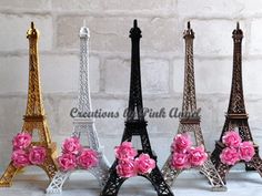 four miniature eiffel tower with pink flowers in front of a white brick wall