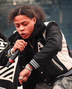 a young man holding a microphone in his right hand and wearing a black jacket with white letters on it