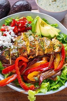 a bowl filled with meat, vegetables and avocado on top of a wooden table