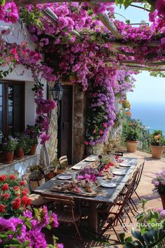 an outdoor dining area with purple flowers growing on the wall and table set for four