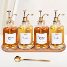 three soap dispensers on a wooden tray with gold spoons next to them