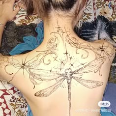 a woman laying on top of a bed with a dragonfly tattoo on her back