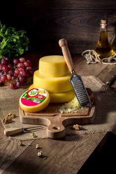 some cheese is on a wooden board with grapes and other food items around the table