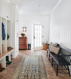 a room with white walls and wooden floors has a large rug on the floor next to a bench