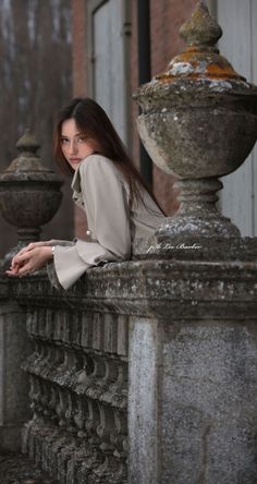 a woman leaning on a stone fence in front of a building