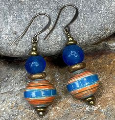 This is a lovely pair of African earrings, created with blue and orange Ugandan paper beads along with blue Ghana glass beads. This set of earrings makes a wonderful personal gift for that special woman who likes a certain unique flare to her jewelry! It can be gifted for any occasion and pairs well, with many different styles of clothing... From casual daytime wear to a sophisticated accessory for evening. The gentle  ear wires, and the paper beads make this set of earrings very lightweight, in spite of their "statement" appearance.  COUPON CODES: Save 10% on purchases totaling $100 or more- enter coupon code 'SAVE10PERCENT' at checkout! Save 15% on purchases totaling $200 or more- enter coupon code 'SAVE15PERCENT' at  checkout! Follow my jewelry on Facebook at "African Echoes Beads" Foll Beaded Jewelry Necklaces, African Earrings, Paper Beads, How To Make Beads, Beaded Earrings, Women's Earrings, My Jewellery, Jewelry Gifts, Beaded Jewelry