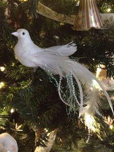 a white bird ornament hanging from a christmas tree with ornaments on it's branches