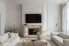 a living room with white couches and a tv mounted on the wall above a fireplace