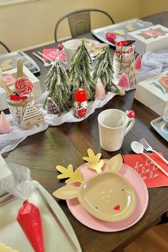 a wooden table topped with plates and cups filled with candy canes next to small christmas trees