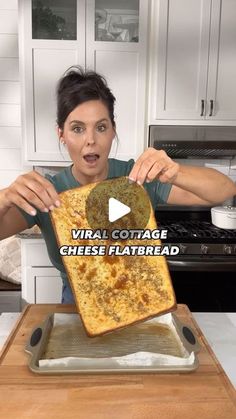 a woman holding up a large piece of bread on top of a pan in the kitchen