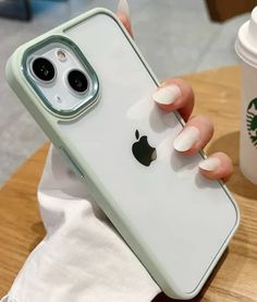 a person holding an iphone in their left hand while sitting at a table next to a cup