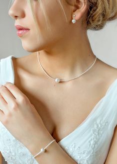 a woman in a white dress wearing a necklace and bracelet with pearls on the neck