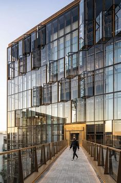 a person walking across a walkway in front of a building with glass walls and balconies