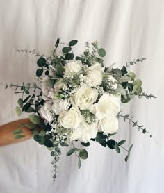 a bouquet of white flowers and greenery is held by a person's arm