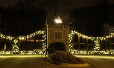 a clock tower with christmas lights on it's sides in front of a gate