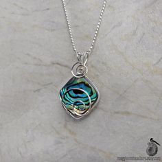 "A square piece of green-blue abalone shell is held tight by sterling silver spirals in this wire wrapped pendant. The shimmery abalone (also called paua) shell is a beautiful sea-foam green with brown concentric patterns like rippling waves. It has flashes of blue and gold and even a subtle violet that skitter across the iridescent surface as it moves on the wearer. The bright silver spirals balance the brown lines and emphasize the watery feel of the colors and movement of light. It's by no me Wire Wrapped Abalone Shell Jewelry For Gifts, Abalone Necklace, Paua Shell, Silver Chain Style, Sterling Silver Wire Wrap, Gold Paper, Wire Wrapped Necklace, Shell Necklace, Metallic Blue