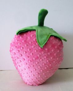 a pink stuffed strawberry with green leaves on it's tip, sitting on a white surface