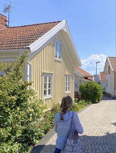 a woman walking down a cobblestone street carrying a bag with writing on it