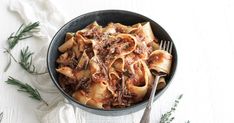 a black bowl filled with pasta and meat on top of a white table next to a fork