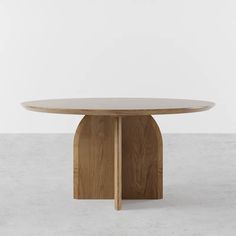 a round wooden table sitting on top of a cement floor next to a white wall