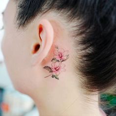 a woman's behind the ear has a small flower tattoo on her left side