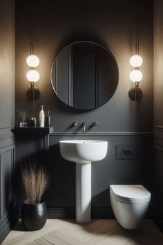 a white toilet sitting next to a sink in a bathroom under two lights on the wall