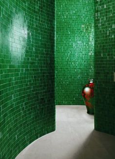 a green tiled bathroom with a red vase in the corner